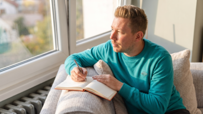 Man writing in a journal by a sunlit window, taking real action rather than just visualising, representing practical manifestation through doing not just wishing