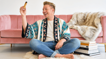 Michael from Woo and Wonder sitting cross-legged holding Palo Santo with a genuine laugh, surrounded by books, representing the real and joyful practice of working with the Lionsgate Portal energy