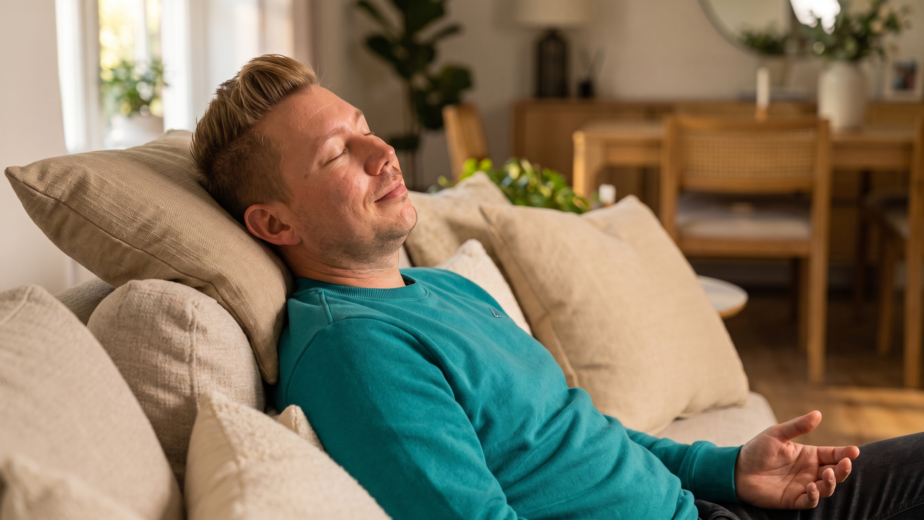 Man resting on a sofa with eyes closed and a peaceful expression, representing the honest exhaustion of spiritual growth and the importance of rest and integration in the awakening process