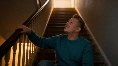 Man sitting on the bottom step of a staircase looking thoughtfully downward with the stairs visible behind him, representing the false start feeling in spiritual growth and the understanding that setbacks are part of the spiral not evidence of failure